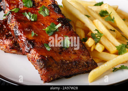 Gegrillte Rippchen serviert mit Pommes frites Close-up auf einem Teller auf den Tisch. Horizontale Stockfoto