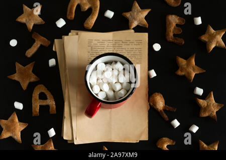 Ansicht von oben flach Ingwer Cookies wie Sterne und Buchstaben frohe Weihnachten und rot Tasse mit Marshmallows auf einem schwarzen Hintergrund geformt Stockfoto