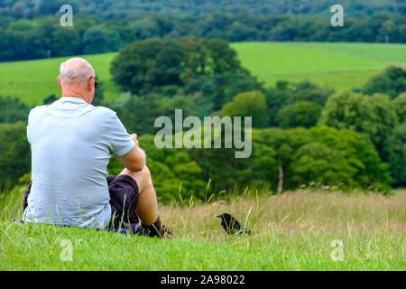 Stockport, Großbritannien - Juli 21, 2019: ein Mann ruht und genießt die Aussicht auf einem Hügel durch eine Krähe im Lyme Park, Peak District, Großbritannien beobachtete Stockfoto