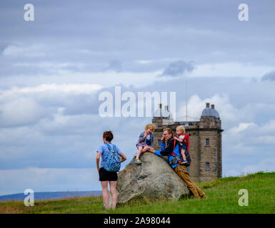 Stockport, Großbritannien - 21. Juli 2019: eine Familie nimmt einen Rest von einem Felsen auf einem Hügel in Lyme Park mit Käfig Turm im Hintergrund Stockfoto