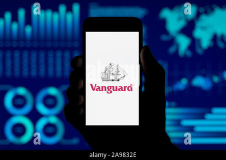 Ein Mann hält ein iPhone, das zeigt die Vanguard Group Logo, Schuß gegen eine Visualisierung von Daten im Hintergrund (nur redaktionelle Nutzung). Stockfoto