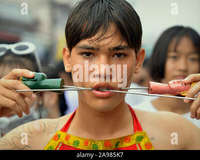 Junge Thai Chinesische taoistische Anhänger durchdringt seine Wangen mit langen Stifte/Spieße während der Phuket Vegetarian Festival (neun Kaiser Götter Festival). Stockfoto