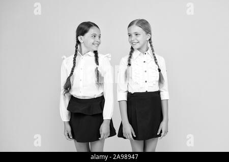 Freundliche Schüler. kleinen Mädchen auf gelben Hintergrund. Freundschaft und Schwesternschaft. beste Freunde. Kid formale Art und Weise. Ausbildung im Ausland. smart suchen Kinder. Schule Freunde. glückliche Kinder in Uniform. Stockfoto