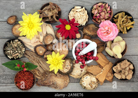 Traditionelle Chinesische Kräuter und Blumen in der Kräutermedizin mit einem Mörser und Pistill aus rustikalem Holz Hintergrund. Stockfoto