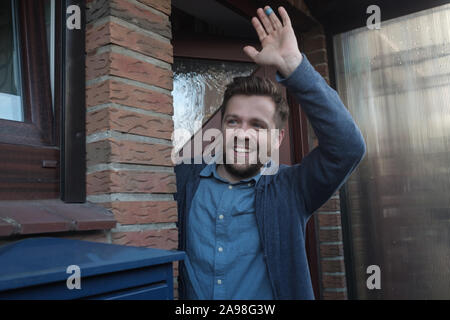Lächelnden jungen Mann winkte mit einem freundlichen fröhlichen Lächeln auf seine neuen Nachbarn. Stockfoto