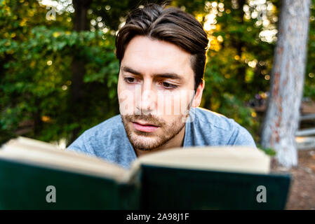 Junger Mann liest eine self-centered Roman in einem Park bei Sonnenuntergang sitzen, genießen der antiken Literatur. Stockfoto