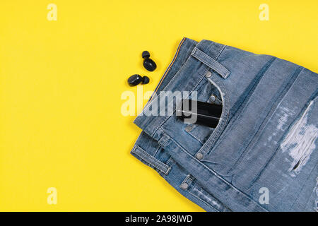 Flach Komposition mit kabellosen Ohrhörern, Jeans und Ladeschale in seiner Tasche auf gelben Hintergrund mit Kopie Raum Stockfoto