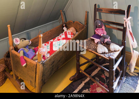 Antike hölzerne Krippe, gewebt Sitz Schaukelstuhl mit dem Kind Puppen im Master Schlafzimmer mit Gelb lackiert breite Diele Dielen in einem alten Haus Stockfoto