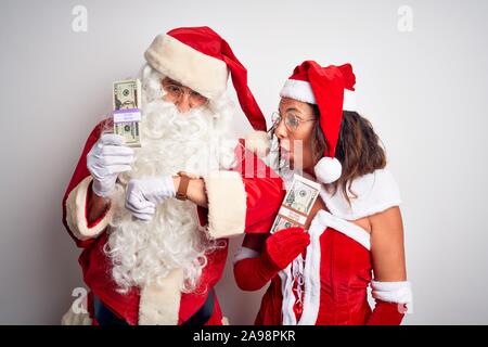 Senior Paar Tragen santa claus Kostüm holding Dollar über isoliert weißer Hintergrund mit Blick auf die Uhr Zeit Sorgen, Angst, sich spät Stockfoto