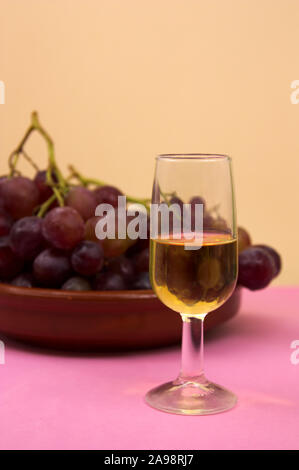 Ein Bild von einem Glas Wein mit den Trauben im Hintergrund in ein Ton Schüssel und ein Pastell Hintergrund, wo Sie Text oder Grafik zu platzieren, kopieren Raum Stockfoto