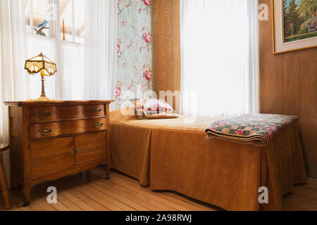 Einzelbett mit gefalteten Decke Decke, antike hölzerne Kommode mit Tiffany Lampe im Schlafzimmer mit Birkenholz Dielen in einem alten 1920er Haus Stockfoto