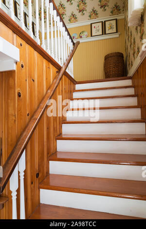 Kiefernholztreppe mit weiß bemalten Balustern, die in die obere Etage in ein altes Haus aus den 1920er Jahren führt. Stockfoto