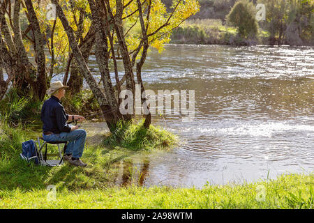 Ältere Menschen im Ruhestand Mann sitzt auf einem Hocker Fischerei auf einem schnell fließenden Fluss Stockfoto