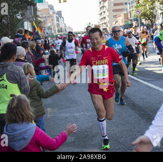 New York City Marathonläufer aus der ganzen Welt durch Nachbarschaft New Yorker entlang der 4th Avenue in Brooklyn, etwa 6 Meile Markierung ermutigt, während der 2019 in New York City Marathon. Lächelnden chinesischen Runner aus China. Stockfoto