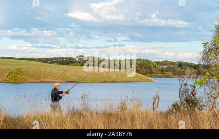 Männliche Rentner Angeln auf den grasbewachsenen Ufern der Hopkins River in Victoria, Australien Stockfoto