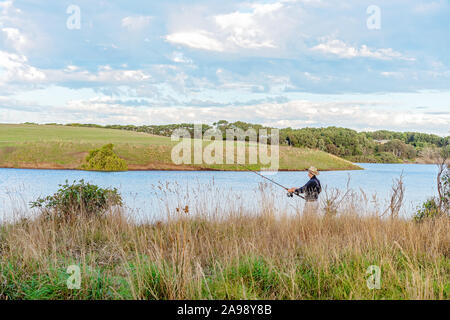 Ältere männliche Fischerei auf einem grasbewachsenen Ufer seinen Ruhestand genießen. Stockfoto