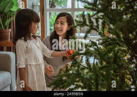 Mutter und Tochter hängen einige Zubehörteile am Weihnachtsbaum Stockfoto