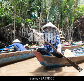 Vietnamesische Frau mit einer konischen Strohhut oder nicht La während Paddeln eine hölzerne Touristenboot im Mekong Delta. Stockfoto