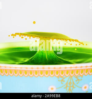 Ein Gelbes und grünes Wasser Tropfen in der Form eines umbrella, in eine dekorative Schale zusammenstieß. Gelb gefärbte Milch fiel in eine grüne Flüssigkeit. Stockfoto