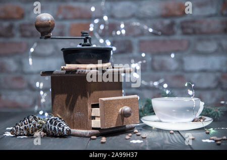 Eine alte manuelle Kaffeemühle und eine Porzellan Schale gegen eine Mauer. Neue Jahr im Loft-Stil. Stockfoto