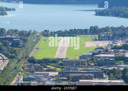 Areal Blick auf den Flughafen Lugano-Agno Landebahn an einem sonnigen Tag mit den Luganer See im Hintergrund Stockfoto