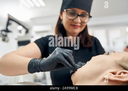 In der Nähe der weiblichen Zahnarzt in Schwarz medizinische Gummihandschuhe holding Instrument und Prüfung der Zähne des Mädchens. Arzt tragen in schwarzen Uniform und medizinische schwarze Kappe. Konzept der Zahnpflege. Stockfoto