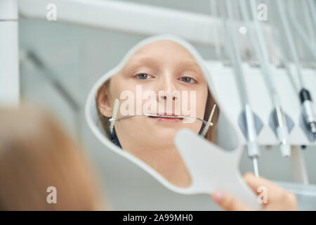 Hübsches Mädchen besuchen Zahnarzt. Jung, hübsch Patienten der Stomatologie Klinik sitzen im Stuhl und Spiegel in Form von Zahn. Schönes kind Zähne Inspektion für die Ausrichtung. Stockfoto