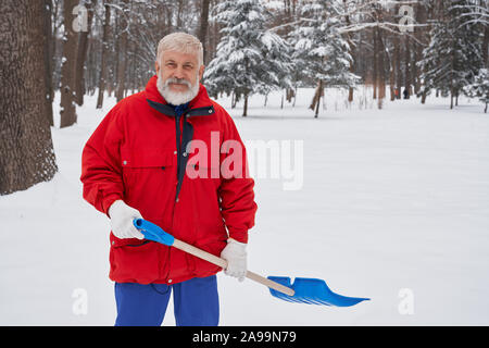 Stadt Service Reinigung Schnee Winter mit Schaufel nach dem Schneesturm. Vorderansicht der älteren sauberer halten Schaufel, an der Kamera schaut. Arbeitnehmer Kleidung in Rot winter Jacke. Stockfoto