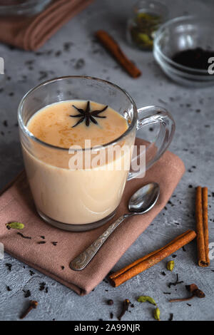 Masala Chai. Indische schwarzer Tee mit Gewürzen und Milch in ein Glas Schale auf einem grauen Hintergrund. Vertikale Foto, close-up. Stockfoto