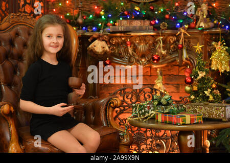 Portrait von Happy girl in der Nähe von Weihnachten Baum sitzen und Tee trinken. Stockfoto