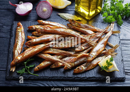 In der Nähe von kalten geräucherten schmilzt auf schwarzem Schiefer Fach mit frischer Petersilie und Zitrone Keile, auf einer hölzernen Tabelle, Ansicht von oben Stockfoto