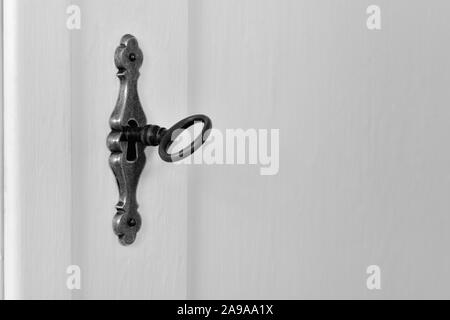 Alte vintage Schlüssel in das Schlüsselloch eines ornamentalen Messing Sperren eines weißen Holzschrank Tür. Schwarzweiß, schwarz-weiß, Antik, kopieren. Stockfoto