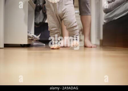 Baby weg von Mutter. kleinen Spaziergang auf Schlafzimmer mit Holzboden. Mutter sitzen warten. warmen liebevollen Familie Konzepte. glückliche Momente der Kinder Stockfoto