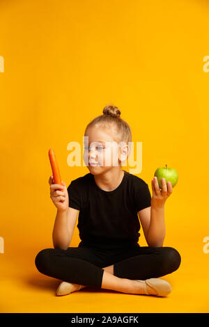 Kleine Tänzerin die Wahl zwischen Karotten und grünem Apfel verwirrt Stockfoto