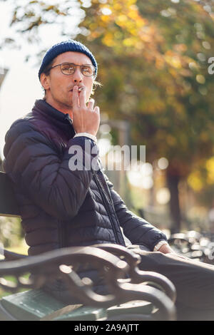 Junger Mann in einem Gap Rauchen einer Zigarette auf einer Bank, während ein schöner Herbsttag. Stockfoto