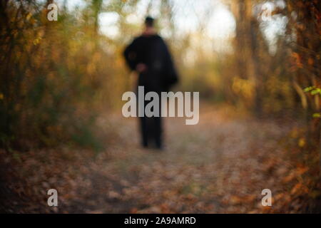 Spaziergang durch die sonnigen Herbst Wald. Silhouette eines einsamen Mann in Schwarz zu Fuß auf der herbstlichen Straße Stockfoto
