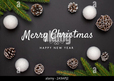 Frohe Weihnachten und guten Rutsch ins Neue Jahr Grußkarte auf der schwarzen Oberfläche von Weihnachtsschmuck umgeben. Stockfoto