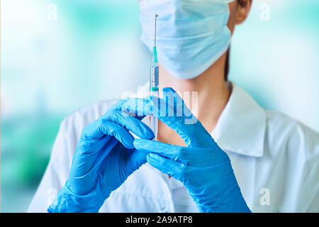 Ärztin oder Wissenschaftlerin in Weiß medizinische Kleid, blau Handschuhe, grüne Kappe und Maske hält eine Spritze in der Hand auf weißem Hintergrund. Sie ist bereit zu geben Stockfoto