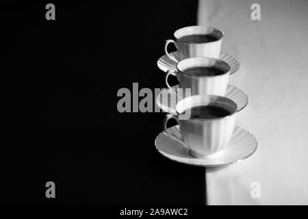 Kaffee Tassen und Untertassen mit schwarzer Tee in einer geraden Linie gefüllt. Stockfoto