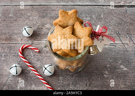 Weihnachtsplätzchen in hausgemachten Glas Glas mit Weihnachtsdekoration, Jingle bells und Candy Cane auf rustikalen, verwitterte, braun Holz Hintergrund der Kontrollleiste. Hohe Stockfoto