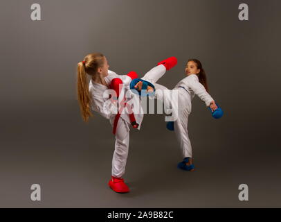 Zwei kleine Karate Mädchen in Kimonos und volle Sport Schutzausrüstung von roten und blauen Kampf gegen einen dunklen Hintergrund Stockfoto