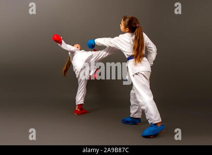 Zwei kleine Karate Mädchen in Kimonos und volle Sport Schutzausrüstung von roten und blauen Kampf gegen einen dunklen Hintergrund Stockfoto