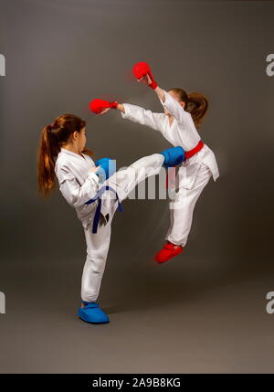 Zwei kleine Karate Mädchen in Kimonos und volle Sport Schutzausrüstung von roten und blauen Kampf gegen einen dunklen Hintergrund Stockfoto