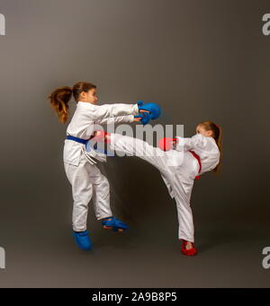 Zwei kleine Karate Mädchen in Kimonos und volle Sport Schutzausrüstung von roten und blauen Kampf gegen einen dunklen Hintergrund Stockfoto