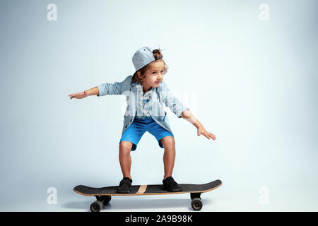 Hübsche junge Junge auf Skateboard in Freizeitkleidung auf weißem Studiohintergrund. Reiten und sieht glücklich aus. Kaukasier Männlich Vorschüler mit hellen Gesichts Emotionen. Kindheit, Ausdruck, Spaß zu haben. Stockfoto