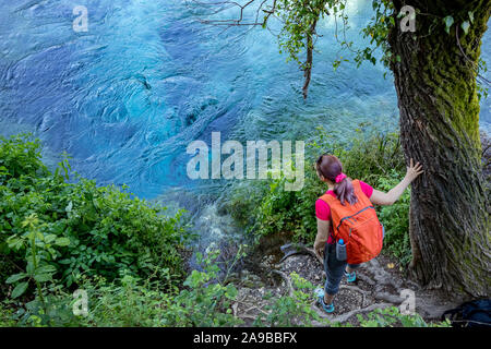 KRONGJI, Albanien - Juni 7, 2019: Junge weibliche Touristen mit orange Rucksack dabei die wunderschönen kristallklaren Fluss Quelle Blau Auge im Wald, Frühling, Albanien. Hohe Winkel, Ansicht von oben Stockfoto