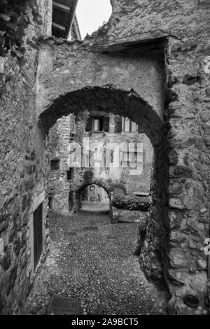 Via Fratelli Bandiera, schmalen Weg durch den Tunnel Bögen in den mittelalterlichen Hill Village von Canale di Tenno, Trentino-Südtirol, Italien. Schwarz und Weiß Stockfoto