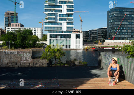 24.06.2019, Berlin, Deutschland - eine Frau, Sonnenbaden am Spreeufer in Friedrichshain. Im Hintergrund ist der lebendige Levels residential Bui Stockfoto