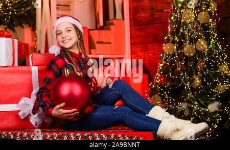 Weihnachten Konzept. Kind Lust Santa genießen Feier ins neue Jahr. Dekor Shop. Lieblingsfarbe. Red Stil. Liebe. Winter Urlaub. Kleines süßes Mädchen mit großen Ball Weihnachtsbaum. Geist der Weihnacht. Stockfoto