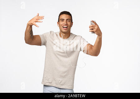 Frech und arrogant cool Hispanic Mann im t-shirt, Händeschütteln und Tanzen, Singen Songs, Verschleiß kabelgebundene Kopfhörer, Smartphone gedrückt halten Stockfoto